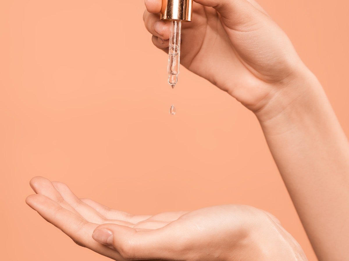 Female hand dropping oil cleanser into amber background, demonstrating skincare routine.