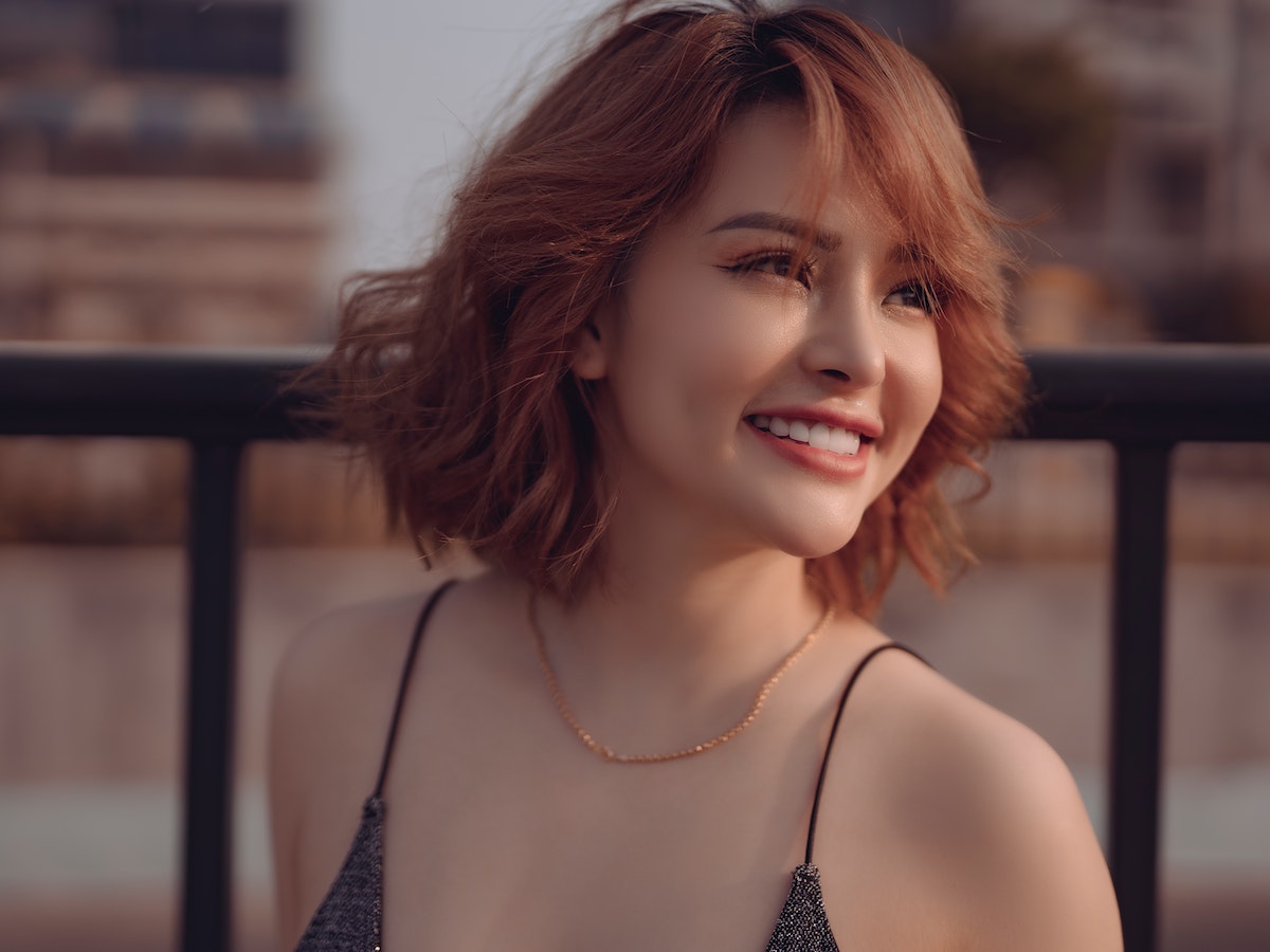 Radiant girl with stunning burgundy hair, showcasing the benefits of Niacinamide with a glowing smile.