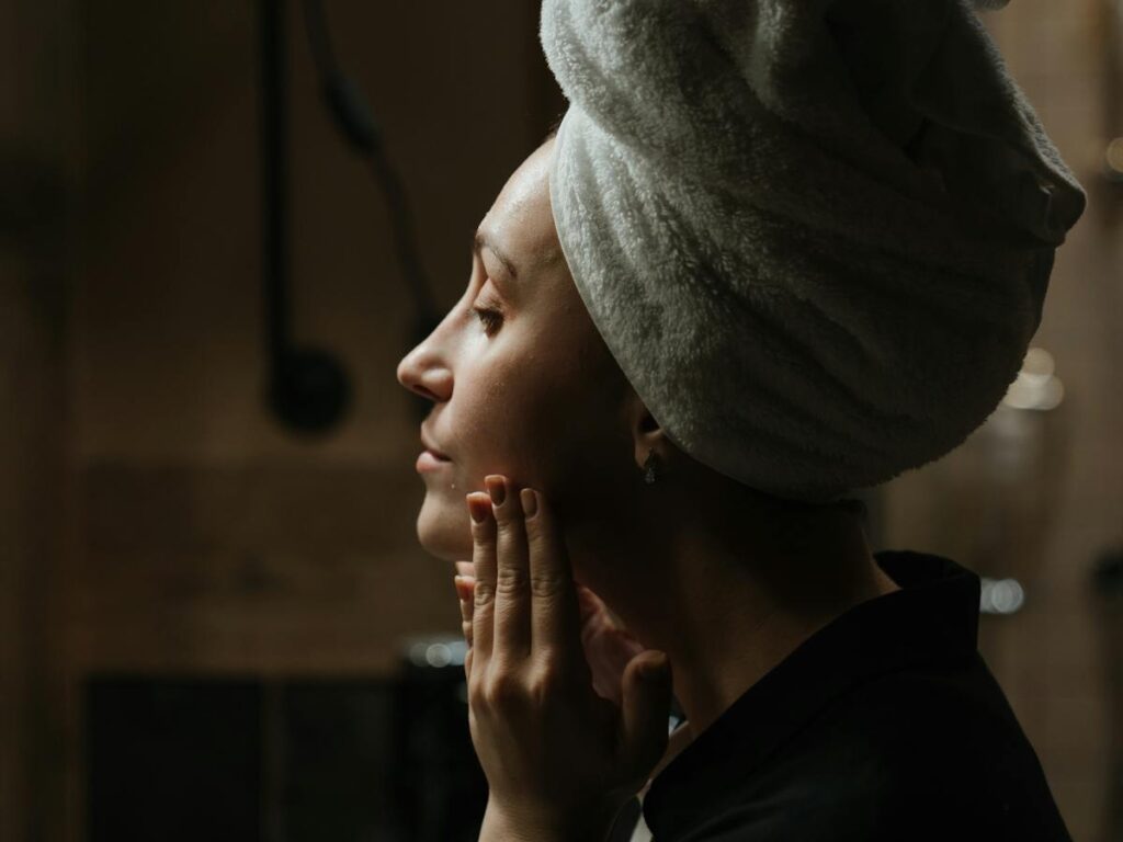 Radiant skincare routine: Woman applying Azelaic Acid Serum, wearing a towel on her head in the bathroom. Elevate your beauty with Azelaic Acid Serum.